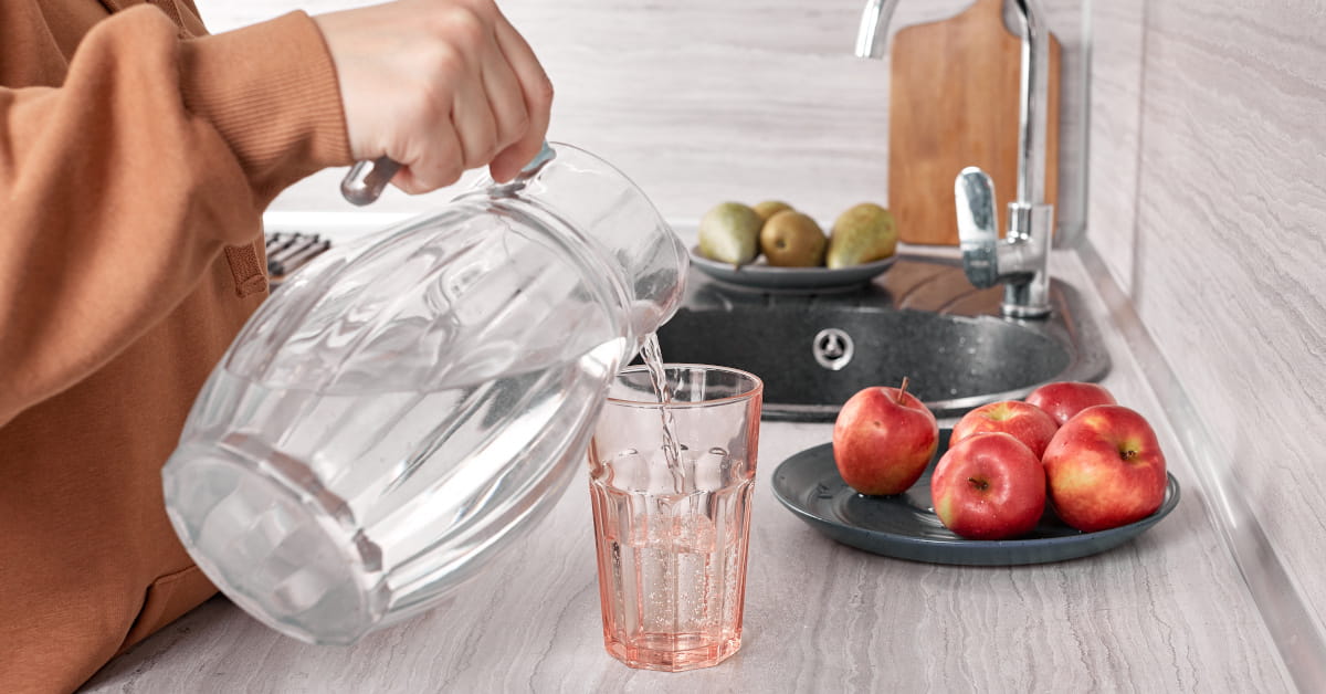 Donna che versa acqua da una caraffa a un bicchiere di vetro